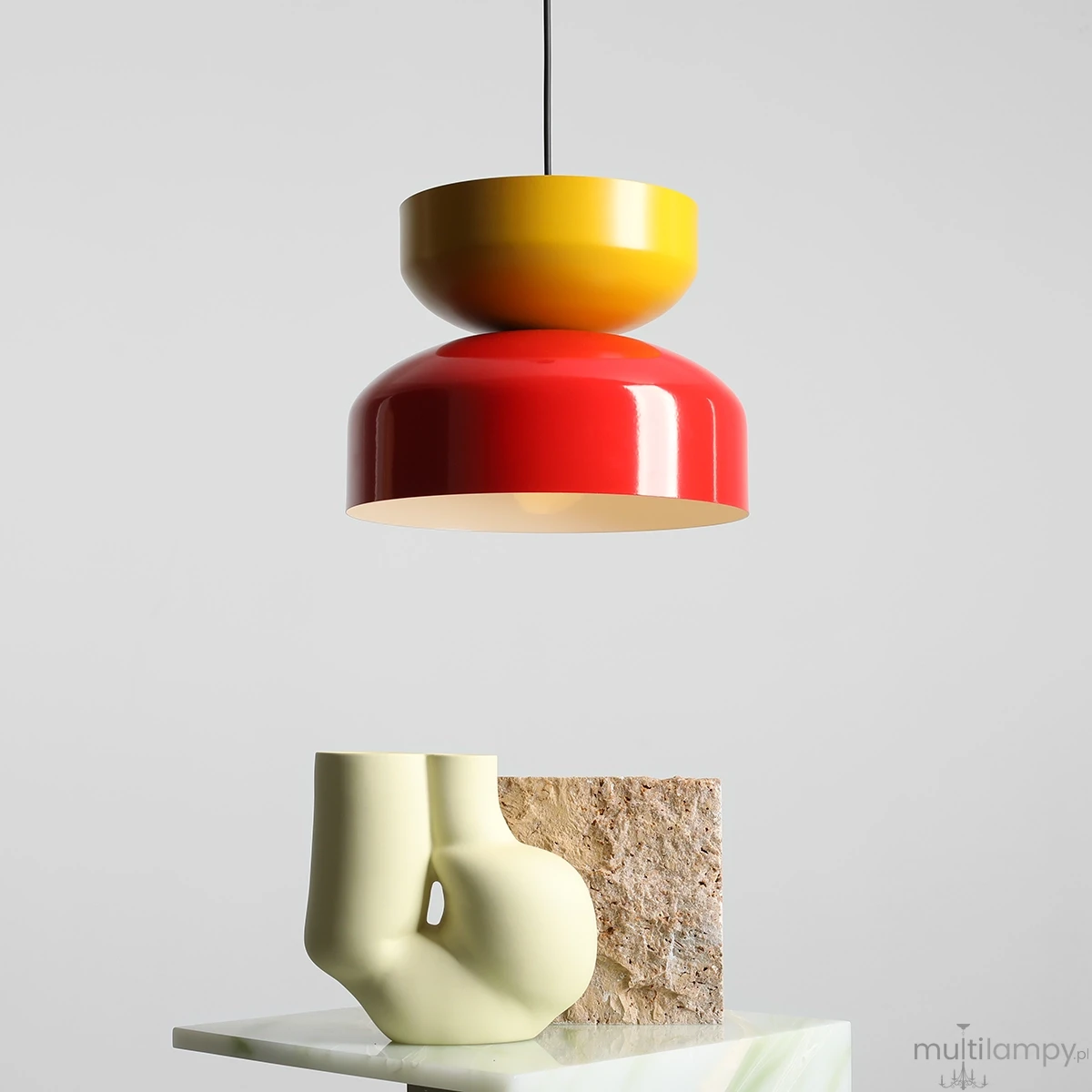 Lampa wisząca Tula w kolorze czerwonym i musztardowym, z okrągłym kloszem i wykończeniem w połysku. Zawieszona na czarnym przewodzie, z minimalistycznym tłem. Stylowy element dekoracyjny w nowoczesnym wnętrzu.