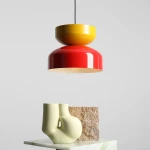 Lampa wisząca Tula w kolorze czerwonym i musztardowym, z okrągłym kloszem i wykończeniem w połysku. Zawieszona na czarnym przewodzie, z minimalistycznym tłem. Stylowy element dekoracyjny w nowoczesnym wnętrzu.