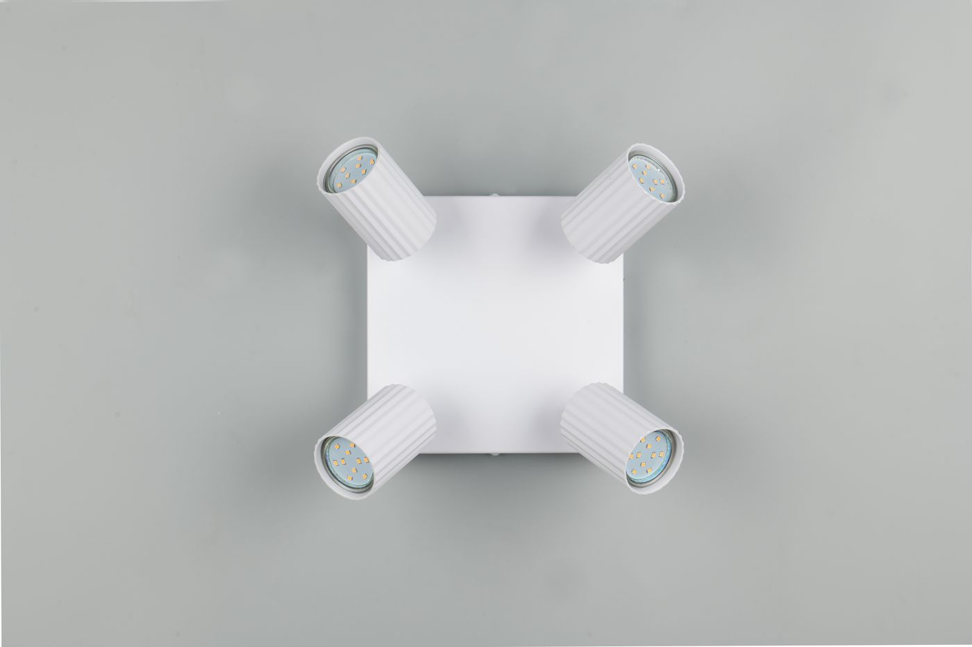 Lampa sufitowa Soka w białym kolorze z czterema ruchomymi reflektorami typu GU10. Kwadratowa podstawa z widocznymi żarówkami w cylindrycznych oprawach o żłobionej fakturze. Zdjęcie z góry, pokazujące równomierne rozmieszczenie źródeł światła.