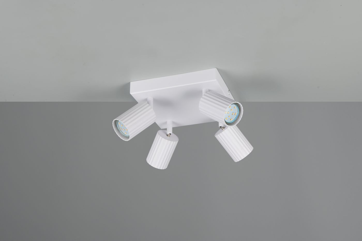 Lampa sufitowa Soka z czterema reflektorami GU10 w białej obudowie. Reflektory mają cylindryczny kształt z rowkowaną fakturą. Ujęcie z góry, ukazujące montaż na suficie, z szarym tłem.