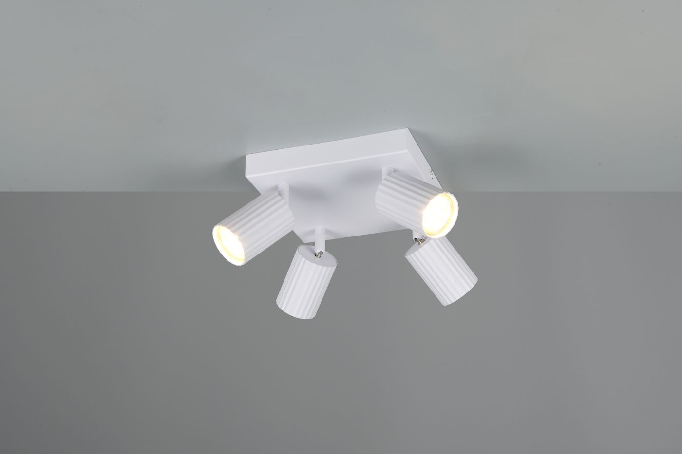 Lampa sufitowa Soka z czterema punktami świetlnymi, w białym kolorze. Reflektory w kształcie cylindrów, umieszczone na kwadratowej podstawie. Kąt ujęcia z góry, ukazujący wszystkie źródła światła. Proste, nowoczesne wzornictwo.