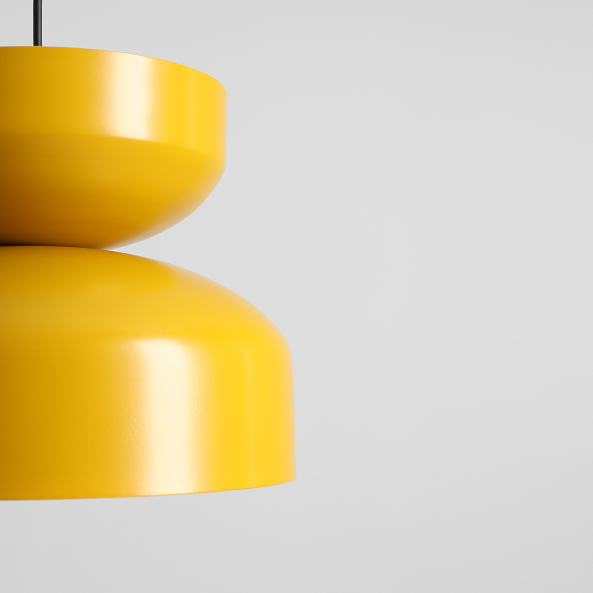 Lampa wisząca Tula w kolorze musztardowym z metalowym kloszem o dwóch zaokrąglonych częściach. Ujęcie z góry, pokazujące detal konstrukcji. Wisi na cienkim przewodzie, na jednolitym tle.