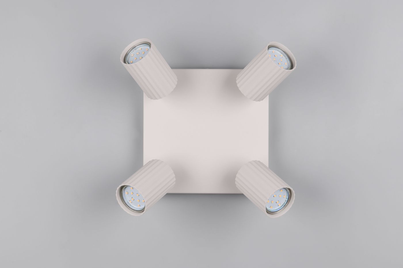 Lampa sufitowa Soka w kolorze szarym z czterema ruchomymi reflektorami GU10. Reflektory mają teksturowane obudowy w kształcie cylindrów. Produkt zamontowany na kwadratowej, płaskiej podstawie. Tło jasnoszare.