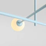 Lampa sufitowa Pinne w kolorze niebieskim z czterema gniazdami E14. Metalowa konstrukcja z pastelowymi elementami, zbliżenie na jeden klosz w kształcie kuli, emitujący ciepłe światło, zawieszony na cienkich rurkach. Tło jasnoszare.