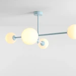 Lampa sufitowa Pinne w kolorze błękitnym, z czterema okrągłymi kloszami w kolorze mlecznym, zawieszona na cienkich metalowych ramionach. Ujęcie z góry pokazujące konstrukcję i detale mocowania sufitowego.