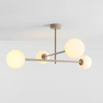 Beżowa lampa sufitowa Pinne z czterema kulistymi kloszami, wykonana z metalu, z zamontowanym centralnym mocowaniem. Klosze w kolorze mlecznym, emitujące miękkie światło, umieszczone na asymetrycznych ramionach. Ujęcie z dołu.