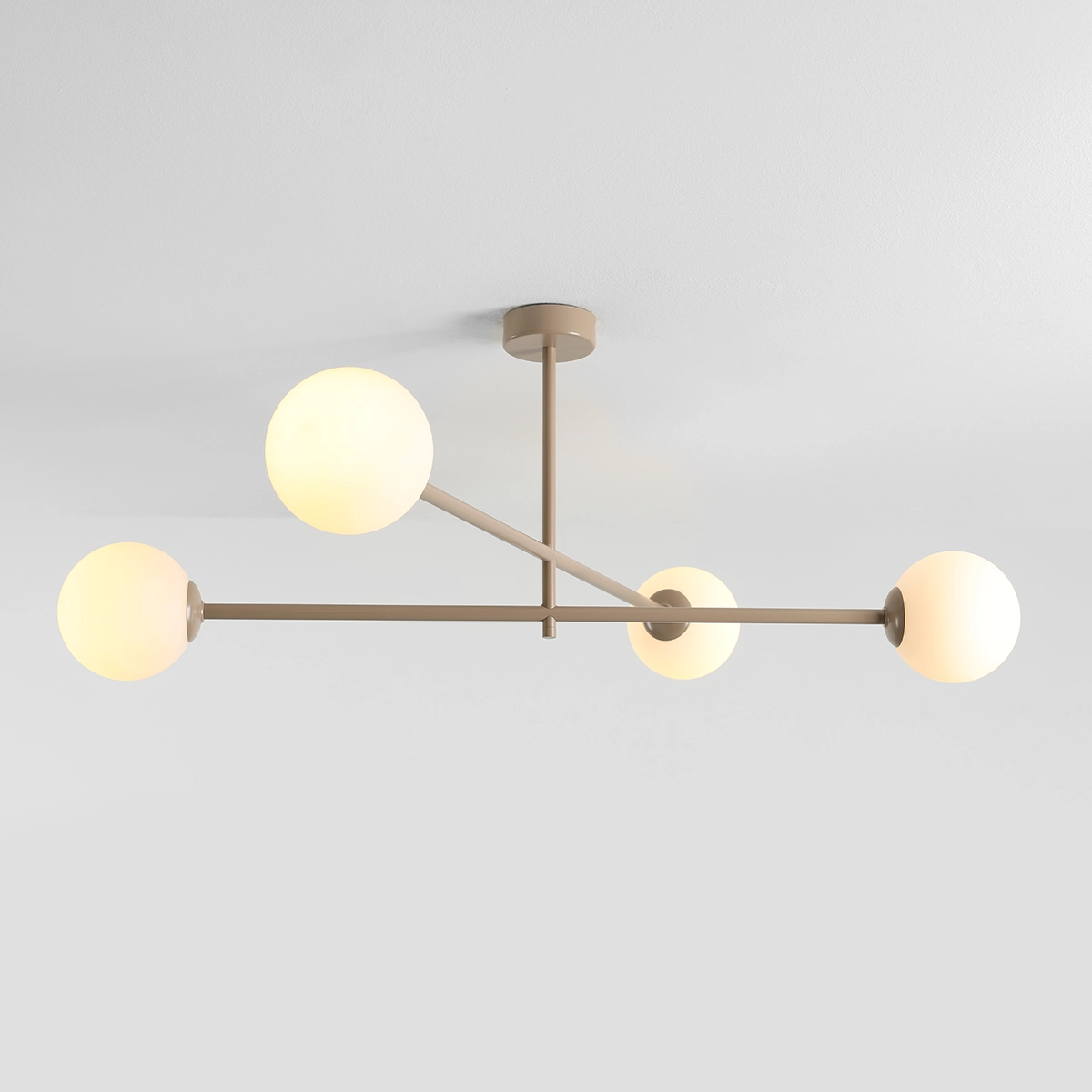Beżowa lampa sufitowa Pinne z czterema kulistymi, mlecznymi kloszami na metalowej konstrukcji. Ujęcie z dołu, pokazujące równomiernie rozmieszczone źródła światła na ramionach lampy. Tło białe, co podkreśla kolor i kształt lampy.