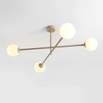 Beżowa lampa sufitowa Pinne z czterema oprawami E14, w kształcie krzyża, z matowym wykończeniem. Szklane klosze w formie kul, umieszczone na cienkich metalowych ramionach. Lampa montowana na suficie, w minimalistycznym stylu.