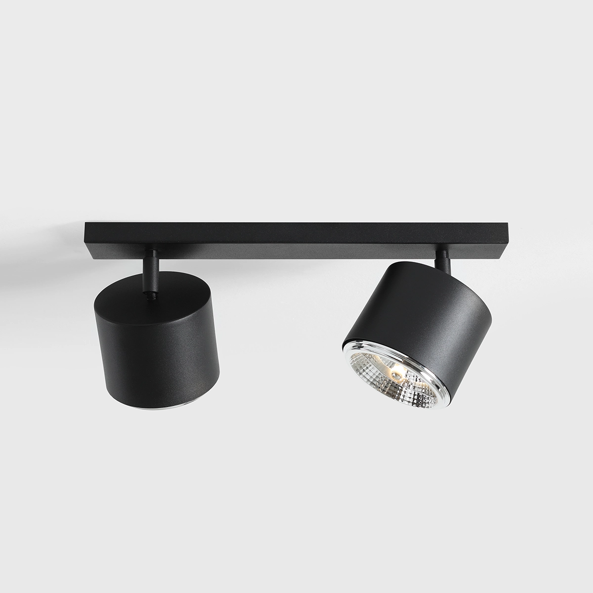 Lampa sufitowa 2-punktowa w kolorze czarnym, zamontowana na prostokątnej, czarnej podstawie. Dwa cylindryczne klosze, jeden z przezroczystym wykończeniem, umożliwiają skierowanie światła w różnych kierunkach. Prosta, nowoczesna forma.