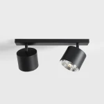 Lampa sufitowa 2-punktowa w kolorze czarnym, zamontowana na prostokątnej, czarnej podstawie. Dwa cylindryczne klosze, jeden z przezroczystym wykończeniem, umożliwiają skierowanie światła w różnych kierunkach. Prosta, nowoczesna forma.