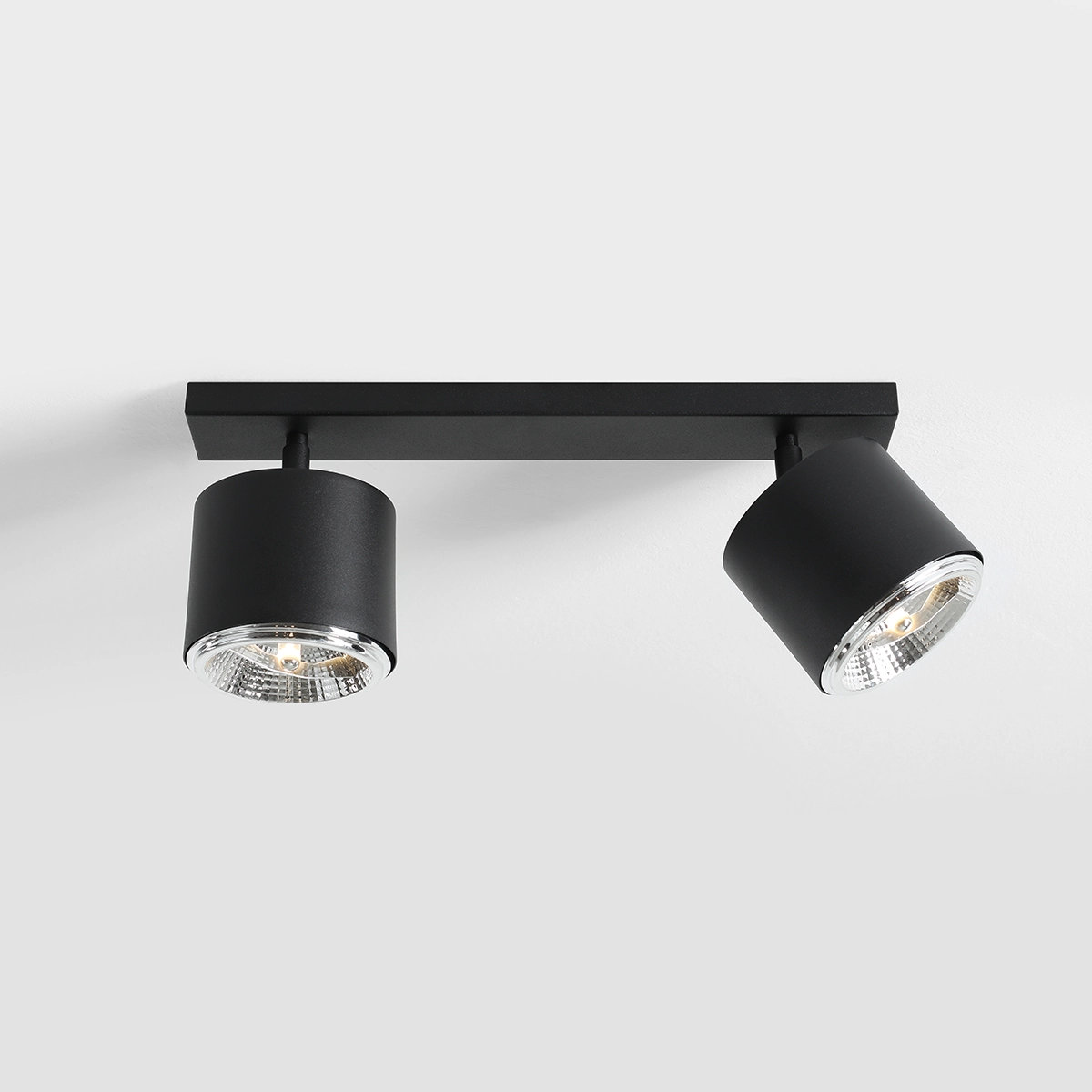 Czarna lampa sufitowa 2-punktowa, z metalowym stelażem i cylindrycznymi oprawami. Ujęcie z dołu, montowana na suficie. Każda oprawa z przezroczystym kloszem, ukazującym źródło światła. Prosty, nowoczesny design, idealna do różnych wnętrz.