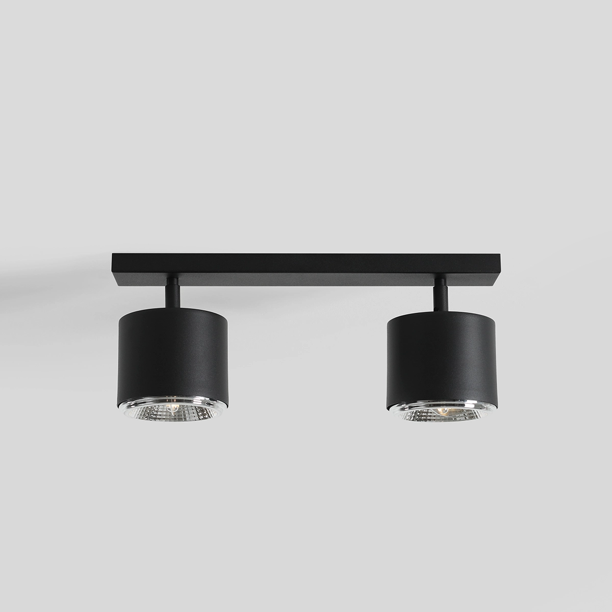 Czarna lampa sufitowa 2-punktowa z metalową konstrukcją, składająca się z dwóch cylindrycznych kloszy z przezroczystymi elementami. Ujęcie frontalne, zamontowana na prostej, płaskiej podstawie. Idealna do nowoczesnych wnętrz.