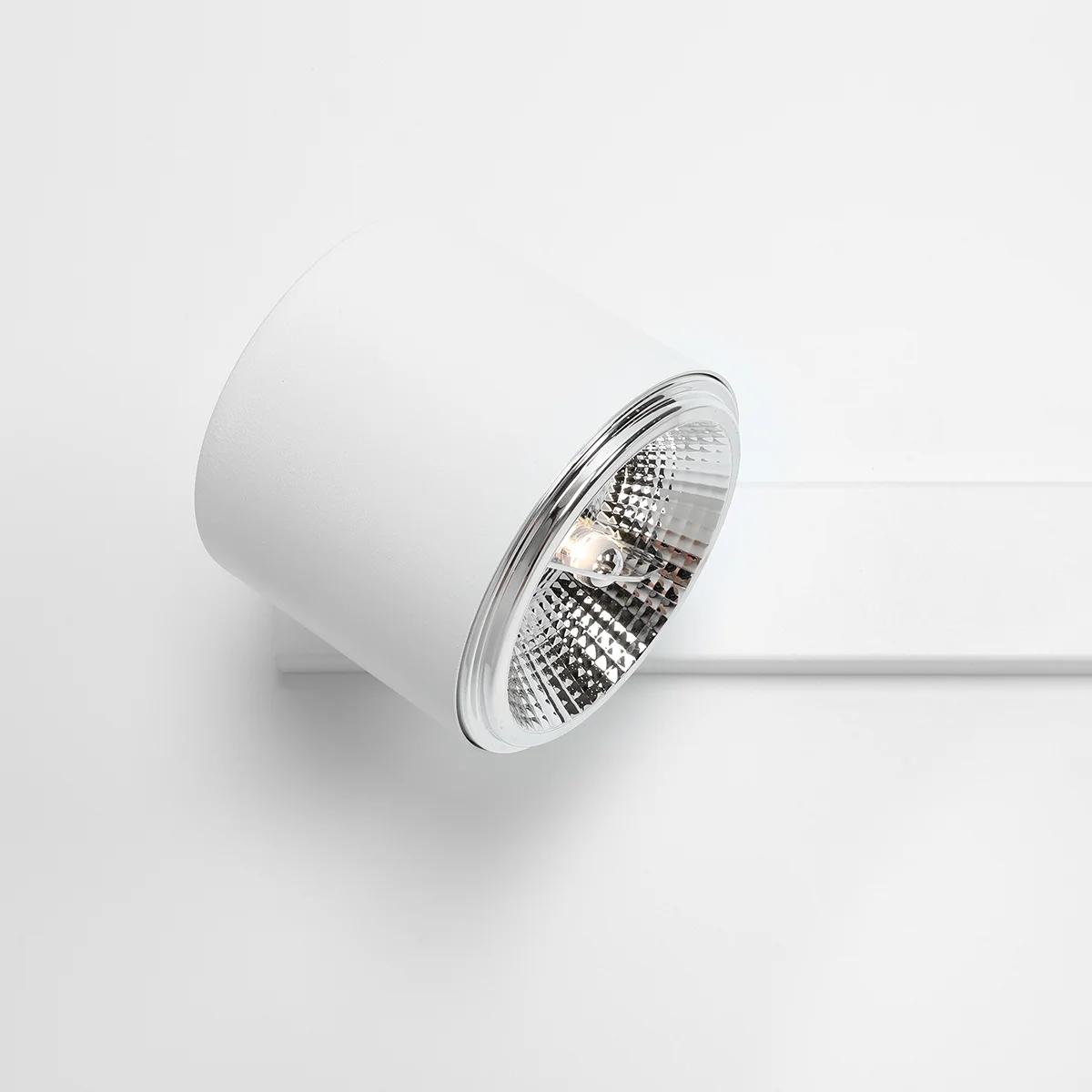 Kinkiet 2-punktowy w kolorze białym z cylindrycznym kloszem, umieszczony na prostej podstawie. Klosz ma lustrzaną wnętrze, co podkreśla źródło światła. Produkt zamontowany na jednolitym, jasnym tle.