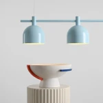 Lampa wisząca Beryl z trzema kloszami E27 w błękitnym kolorze, zawieszona na poziomej rurze. W tle widoczna dekoracyjna misa na okrągłej podstawie. Tło jasnoszare, minimalistyczne.