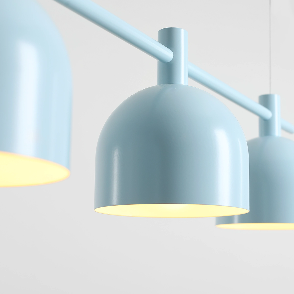 Lampa wisząca Beryl w kolorze błękitnym z trzema kulistymi kloszami zawieszonymi na prostokątnej rurze. Klosze mają matową powierzchnię, a ich wnętrze jest w kolorze żółtym, co podkreśla efekt oświetlenia.