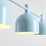Lampa wisząca Beryl w kolorze błękitnym z trzema kulistymi kloszami zawieszonymi na prostokątnej rurze. Klosze mają matową powierzchnię, a ich wnętrze jest w kolorze żółtym, co podkreśla efekt oświetlenia.