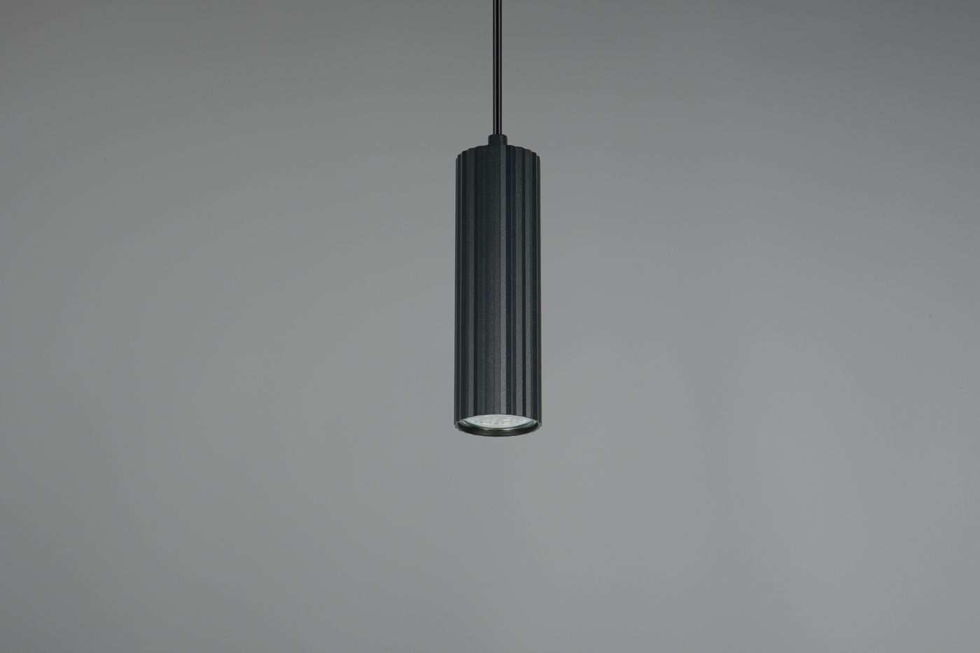 Lampa wisząca Soka w kolorze czarnym, o cylindrycznym kształcie z teksturowanym wykończeniem. Ujęcie frontalne, zawieszona na cienkim przewodzie, z widocznym źródłem światła GU10 na dole. Prosty, nowoczesny design.