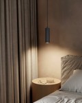 Lampa wisząca Soka 1xGU10 w kolorze czarnym, o cylindrycznym kształcie, zawieszona nad nocnym stolikiem. W tle widoczne zasłony w odcieniu brązu oraz szare pościele na łóżku. Światło skierowane na stół z szklanką i okularami.