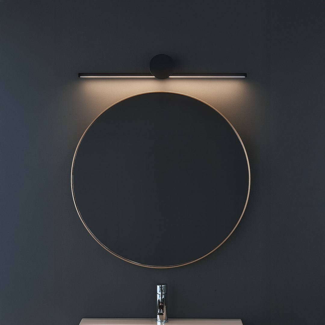 Kinkiet Artist L40,5 LED 6W 4000K w kolorze czarnym, montowany nad okrągłym lustrem. Oświetlenie punktowe, minimalistyczny design, z okrągłym elementem mocującym. Tło w ciemnym kolorze, lampa emituje ciepłe światło.