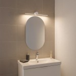 Biały kinkiet Artist L40,5 LED 6W 4000K IP44, zamontowany nad owalnym lustrem. Oświetlenie skierowane na lustro, otoczenie w neutralnych odcieniach szarości. Kinkiet ma minimalistyczny design, zamocowany na gładkiej, jasnej ścianie.