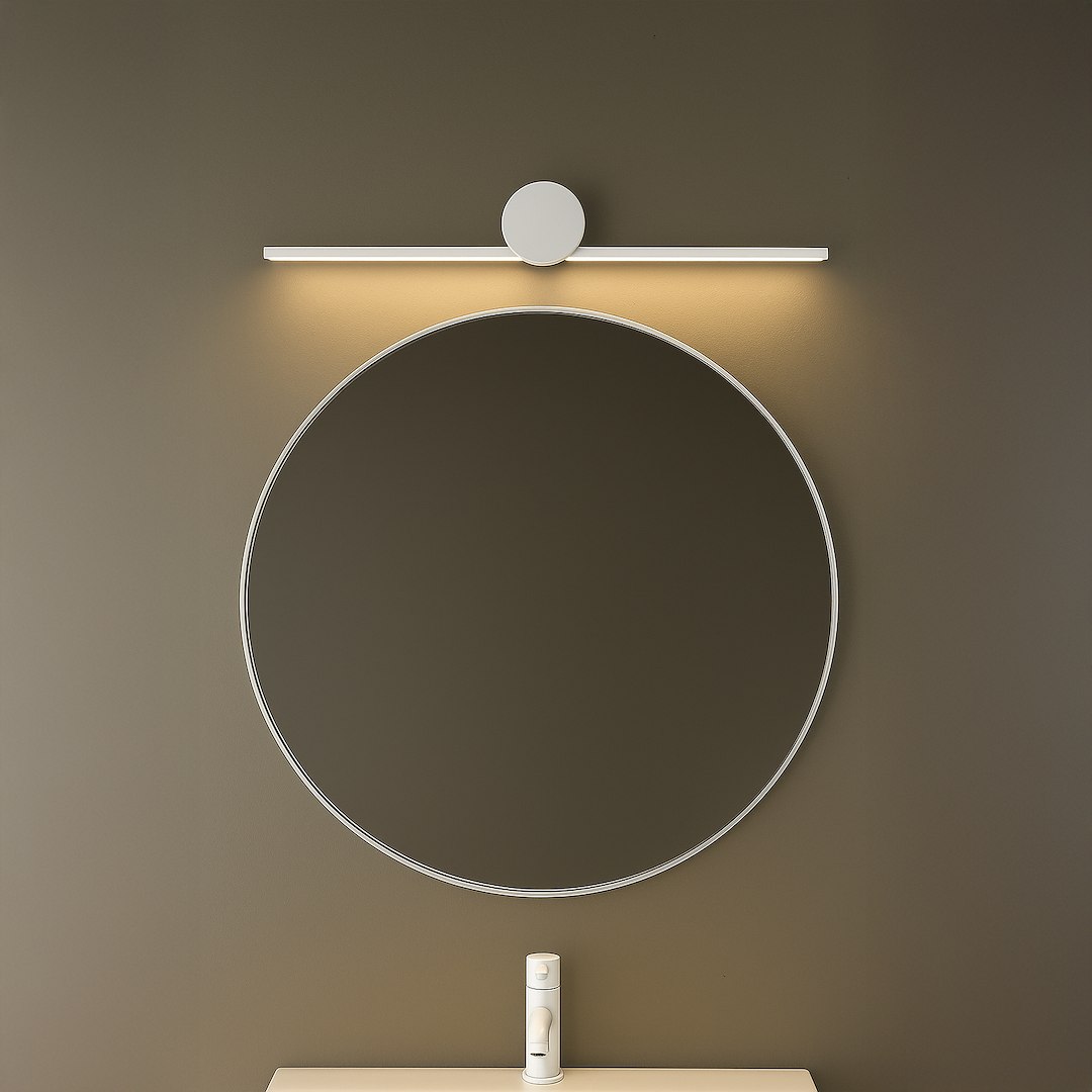 Kinkiet Artist L40,5 LED 6W 4000K IP44 w kolorze białym, zamontowany nad okrągłym lustrem. Lampa ma prostą, minimalistyczną formę z okrągłym elementem na górze i emitującym światło paskiem. Tło w odcieniu brązu.