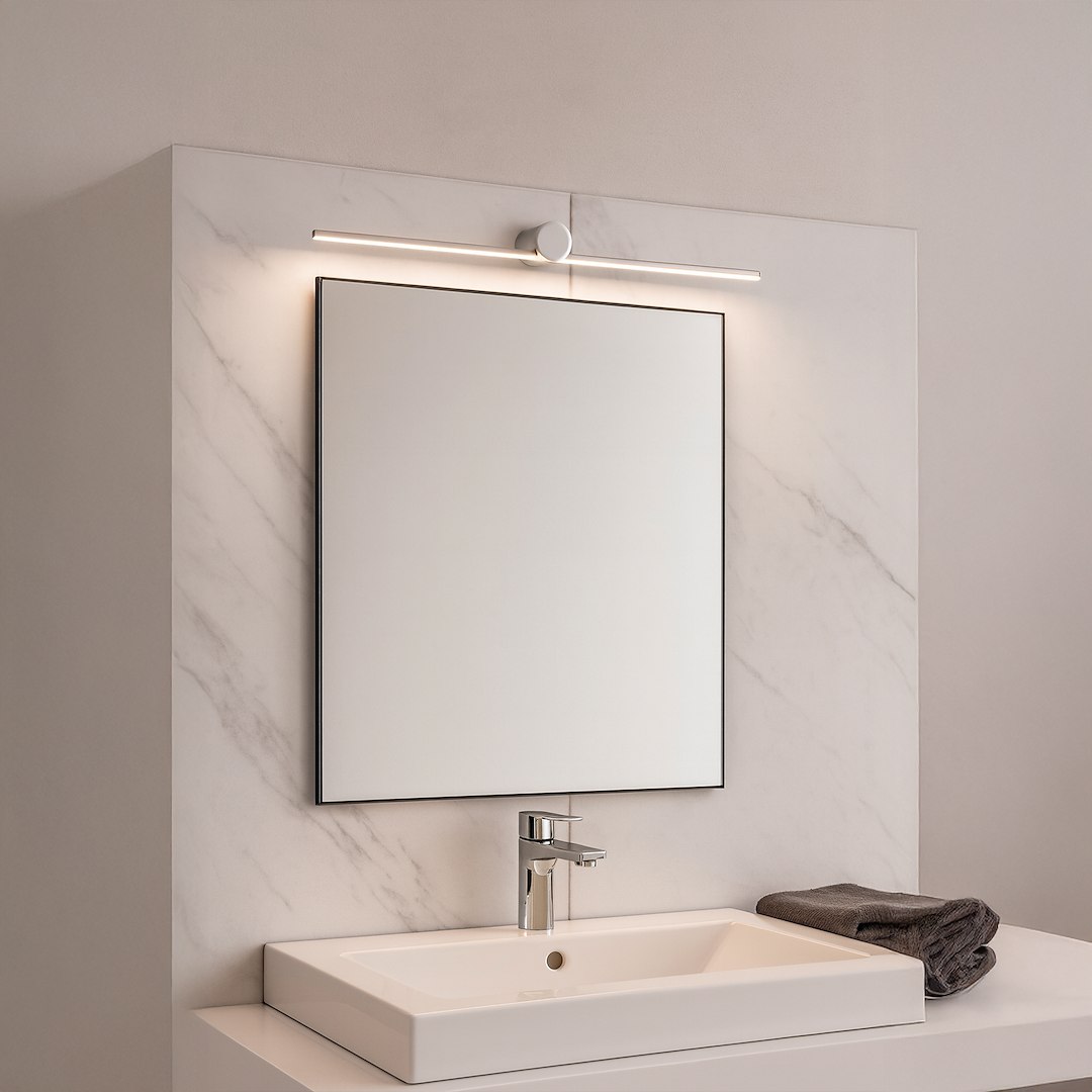 Kinkiet Artist L60,5 LED 9W 4000K IP44 w chromowanej obudowie, zamontowany nad prostokątnym lustrem na marmurowej ścianie. Produkt emituje ciepłe światło, tworząc nowoczesny akcent w łazience. Widoczne umywalka i szare ręczniki w tle.