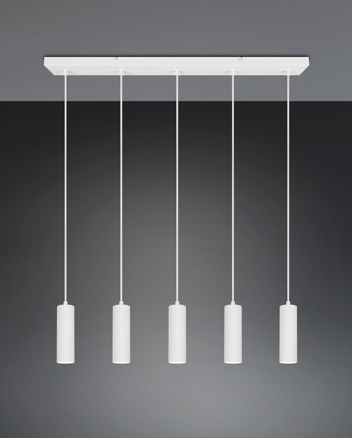 Lampa wisząca Soka z pięcioma oprawami GU10, biała. Zawieszona na prostokątnej podstawie, z cylindrycznymi kloszami o teksturowanej powierzchni. Ujęcie frontalne, na jednolitym ciemnym tle.