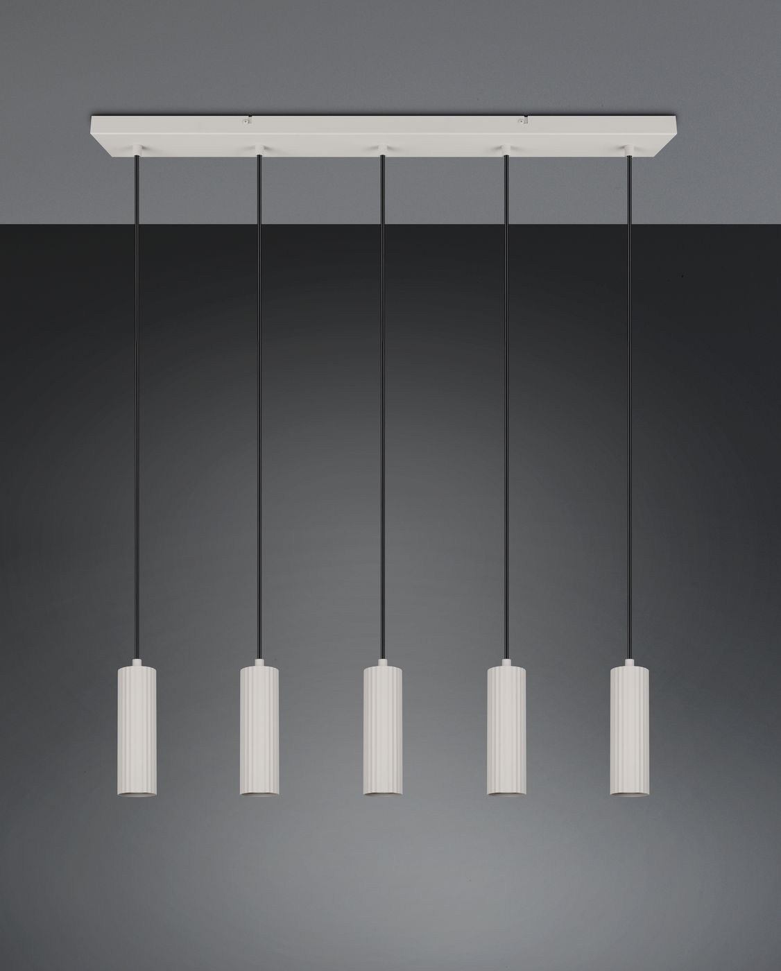 Lampa wisząca Soka z pięcioma oprawami GU10, w kolorze szarym. Posiada cylindryczne klosze z teksturą, zawieszone na czarnych linkach. Ułożenie poziome na białej podstawie, w minimalistycznym stylu, na tle szarej ściany.