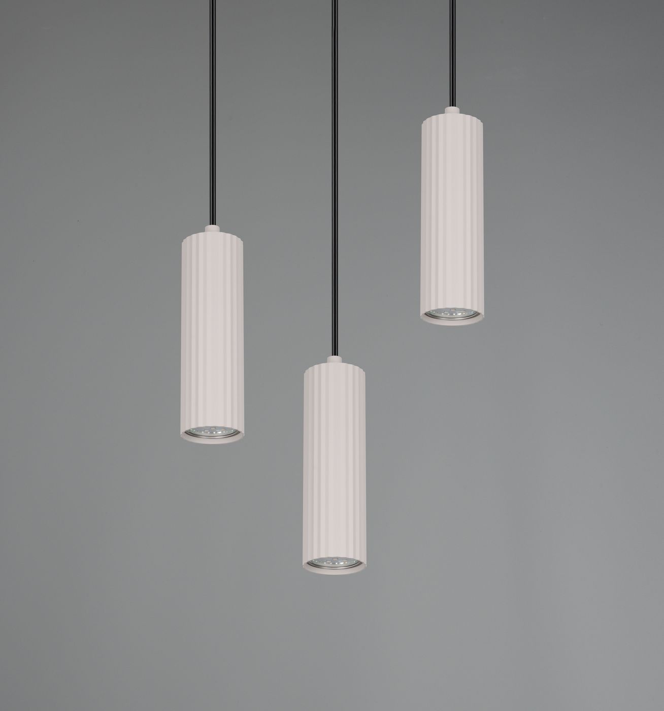 Lampa wisząca Soka z trzema cylindrycznymi kloszami w kolorze szarym, umieszczona na czarnych przewodach. Klosze mają teksturowaną powierzchnię z poziomymi żłobieniami. Produkt zawiera miejsca na żarówki GU10. Tło szare, minimalistyczne.