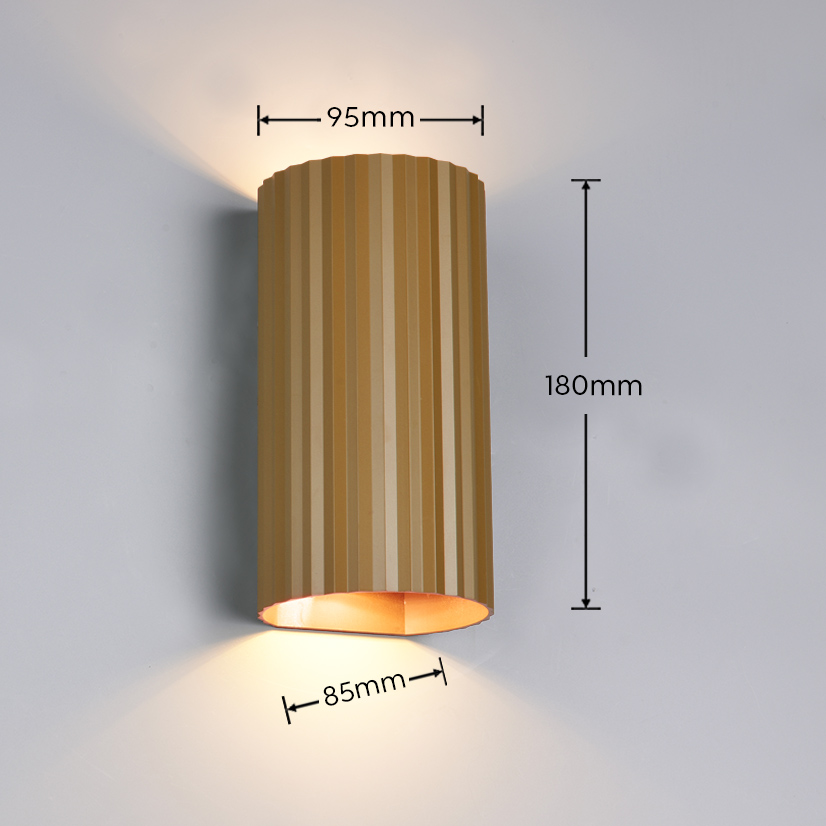 Kinkiet Soka w kolorze kawowym, o cylindrycznym kształcie z żłobieniami. Wymiary: 180 mm wysokości, 95 mm średnicy, 85 mm szerokości. Wbudowane dwa gniazda GU10, emitujące światło w górę i w dół. Montowany na ścianie, w tle jednolita powierzchnia.
