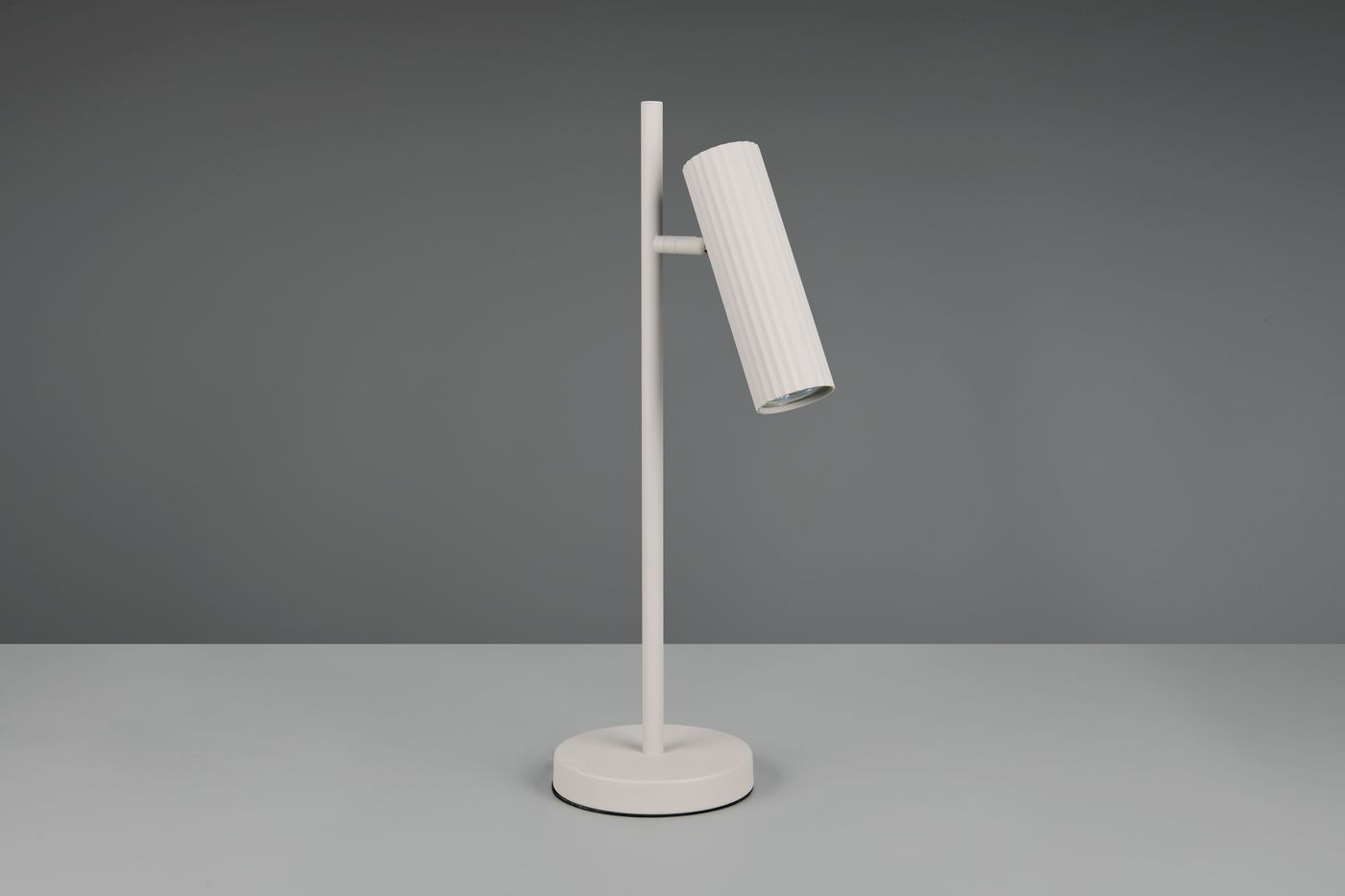 Lampa stołowa Soka, szara, z okrągłą podstawą. Posiada cylindryczny klosz z rowkowaną teksturą, zamontowany na prostym, pionowym stelażu. Ujęcie z boku, ukazujące detal klosza i jego kąt nachylenia.