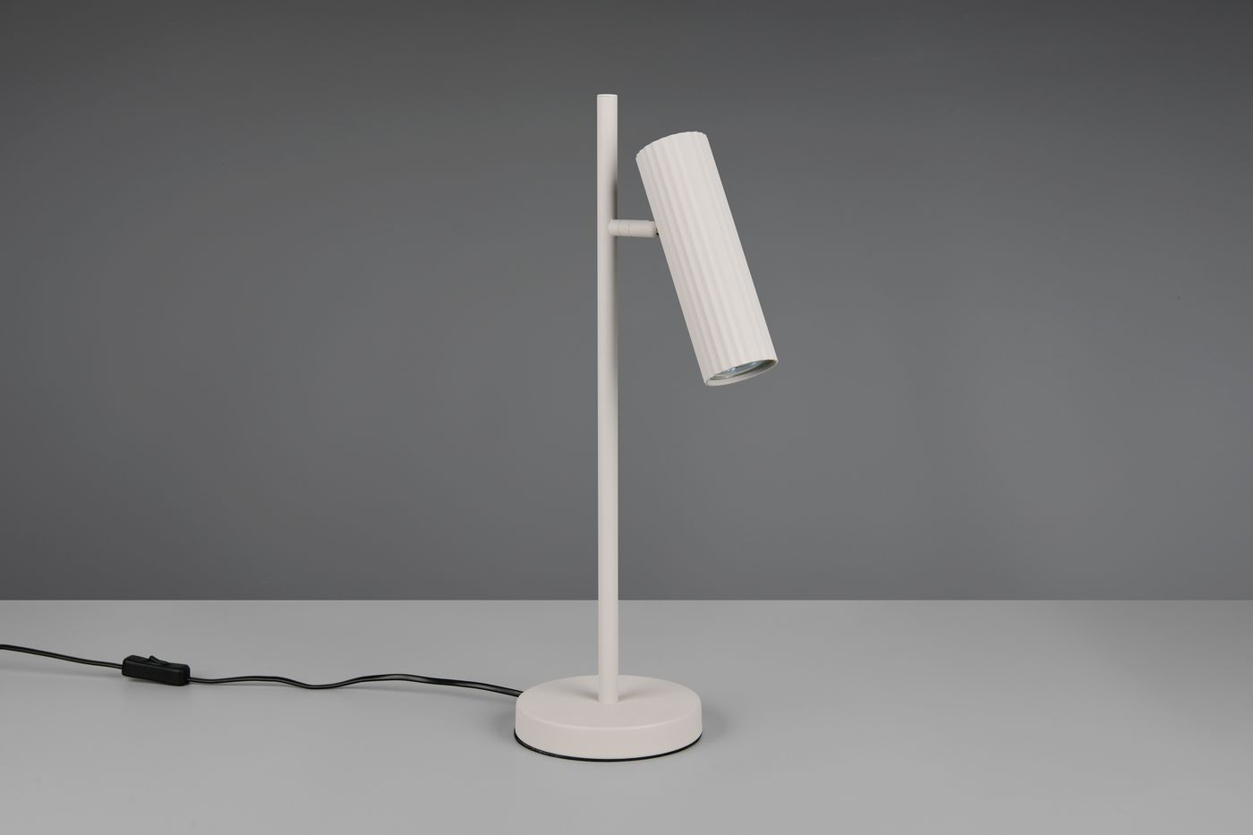 Szara lampa stołowa Soka z jedną oprawą GU10, z prostym, cylindrycznym kloszem o żebrowanej fakturze, umieszczona na okrągłej podstawie. Ujęcie z boku, kabel z włącznikiem widoczny na stole.