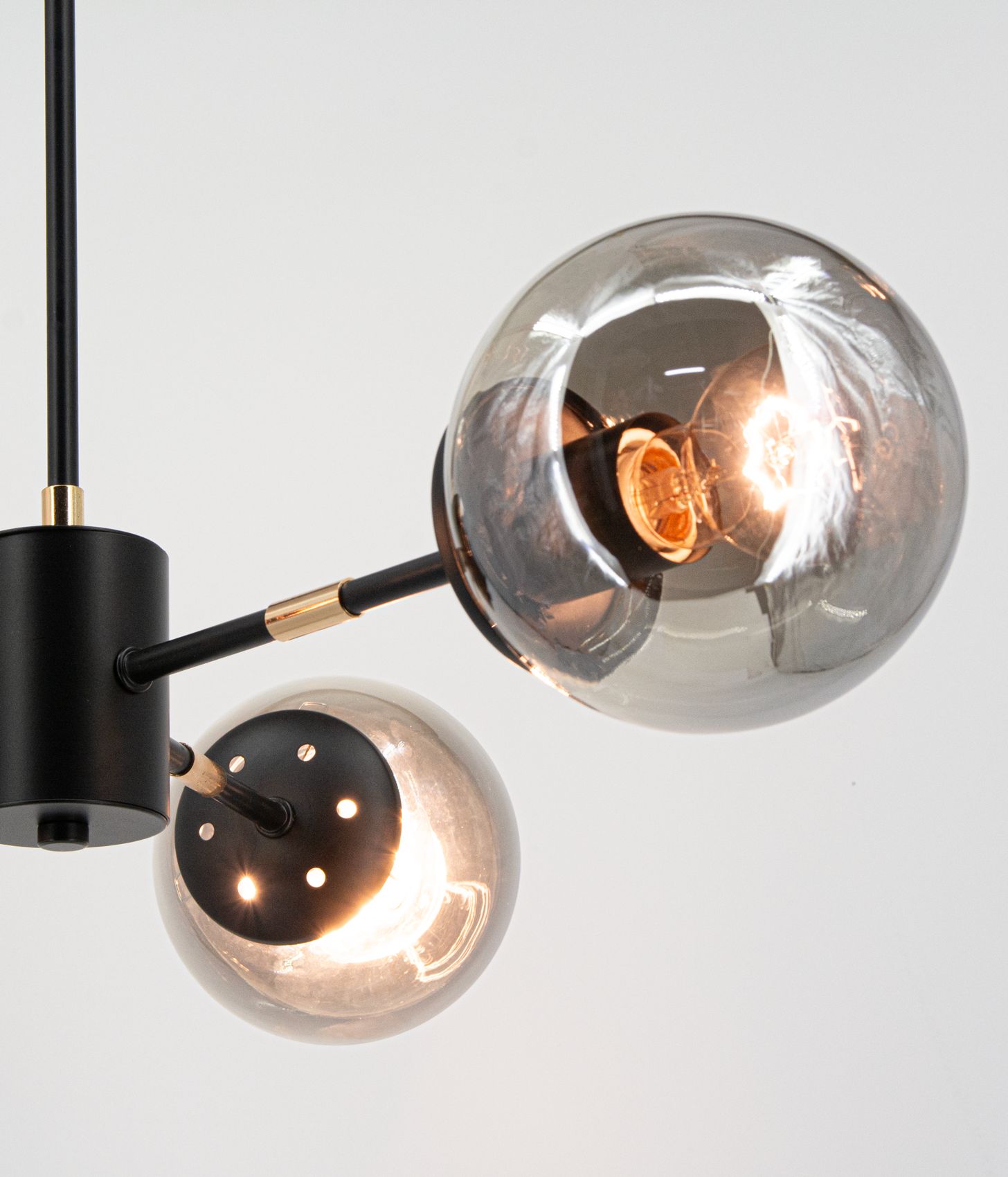 Lampa wisząca Gaja z trzema żarówkami E27 w czarnej i złotej kolorystyce. Elementy metalowe w matowym czarnym wykończeniu, szklane klosze w kształcie kul, z widocznymi żarówkami. Ujęcie z góry, ukazujące detale konstrukcji.