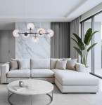 Lampa wisząca Paco z chromowanym wykończeniem, wyposażona w sześć oprawek E14, zawieszona w centralnej części pomieszczenia. W tle widoczny jasny salon z szarym narożnikiem, okrągłym stołem i dużymi oknami.