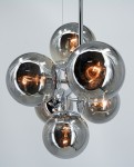 Lampa wisząca Paco z sześcioma kloszami w kształcie szklanych kul, wykonana w chromowanej obudowie. Klasyczny design z widocznymi żarówkami E14, zawieszona na cienkim przewodzie. Tło jasnoszare, co podkreśla elegancję produktu.