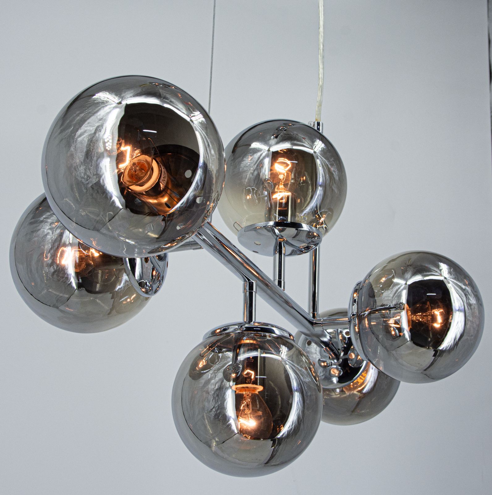 Lampa wisząca Paco z sześcioma kulistymi kloszami w kolorze szarym, wykonana z chromowanego metalu. Ujęcie z góry, pokazujące połączenie kloszy i żarówek E14. Całość zawieszona na białym przewodzie, na jasnym tle.