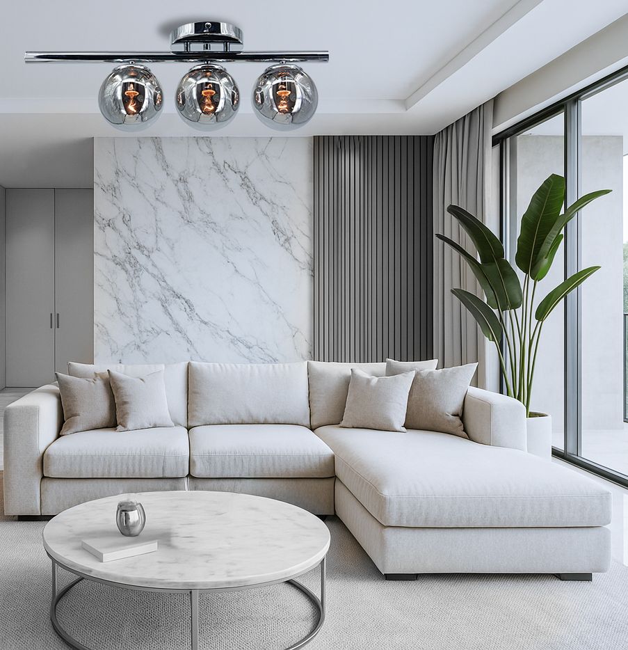 Lampa sufitowa Argo 3xE14 w chromowanej obudowie, z trzema szklanymi kloszami. Ujęcie z góry, zawieszona nad jasną sofą w nowoczesnym wnętrzu z marmurową ścianą i dużymi oknami. W tle widoczna roślina doniczkowa.