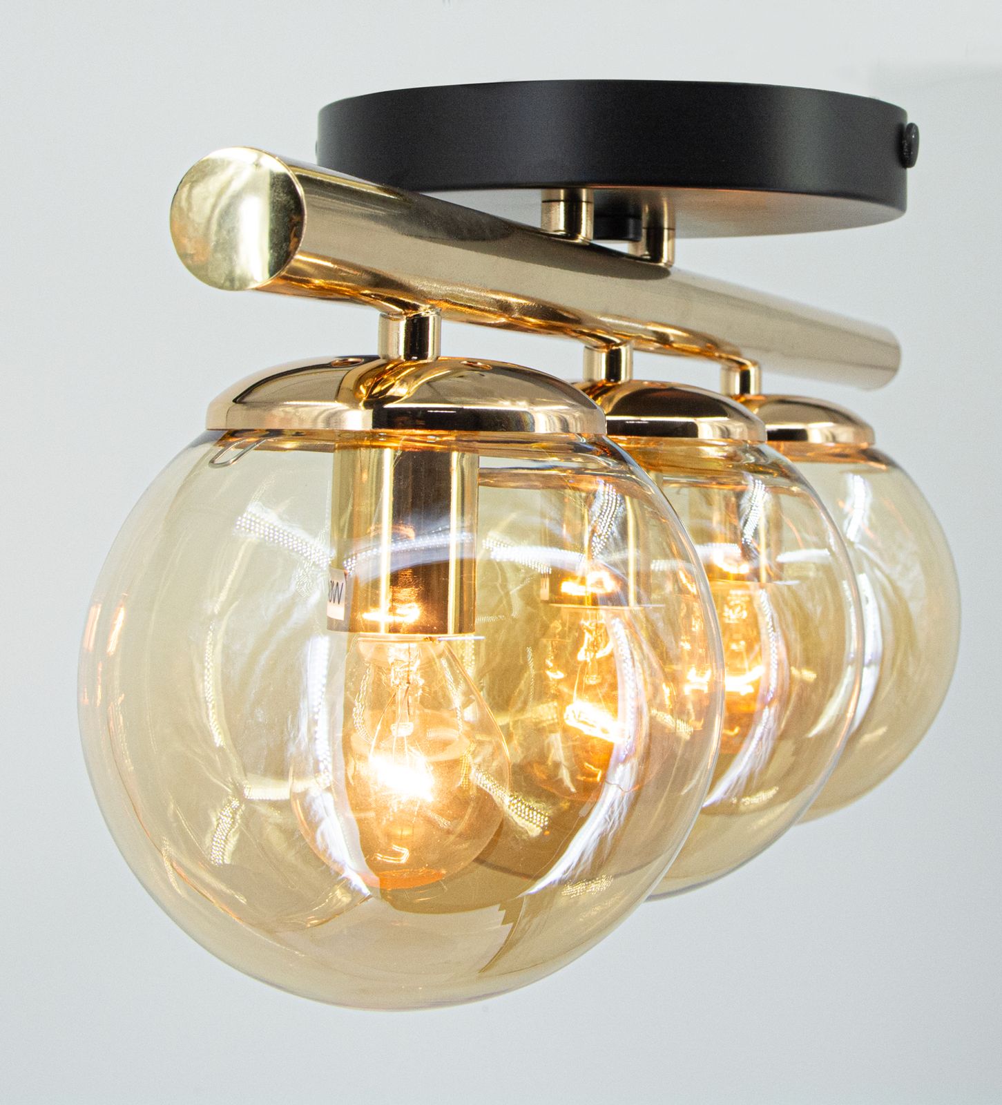 Lampa sufitowa Argo z trzema kloszami E14, złota i czarna. Klosze w kształcie kul, wykonane z przezroczystego szkła, montowane na metalowej, błyszczącej konstrukcji. Widoczna złota podstawa i czarny sufitowy uchwyt.