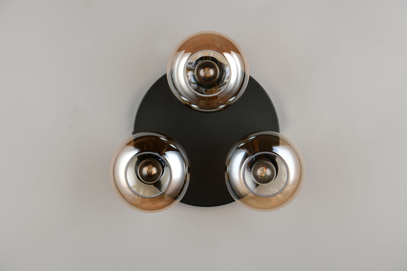 Lampa sufitowa Divina z trzema kloszami E14 w kolorze bursztynowym i czarną podstawą. Klosze mają zaokrąglony kształt, są metaliczne i połyskujące, zamontowane na okrągłej, matowej podstawie. Ujęcie z góry.