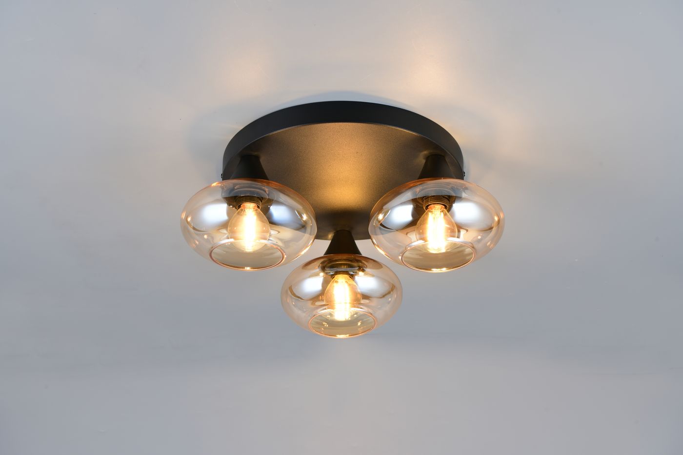 Lampa sufitowa Divina z trzema oprawami E14, w czarnej obudowie, z bursztynowymi kloszami. Ujęcie z dołu, pokazujące wszystkie trzy żarówki. Wykończenie metalowe, z eleganckimi, okrągłymi kloszami.