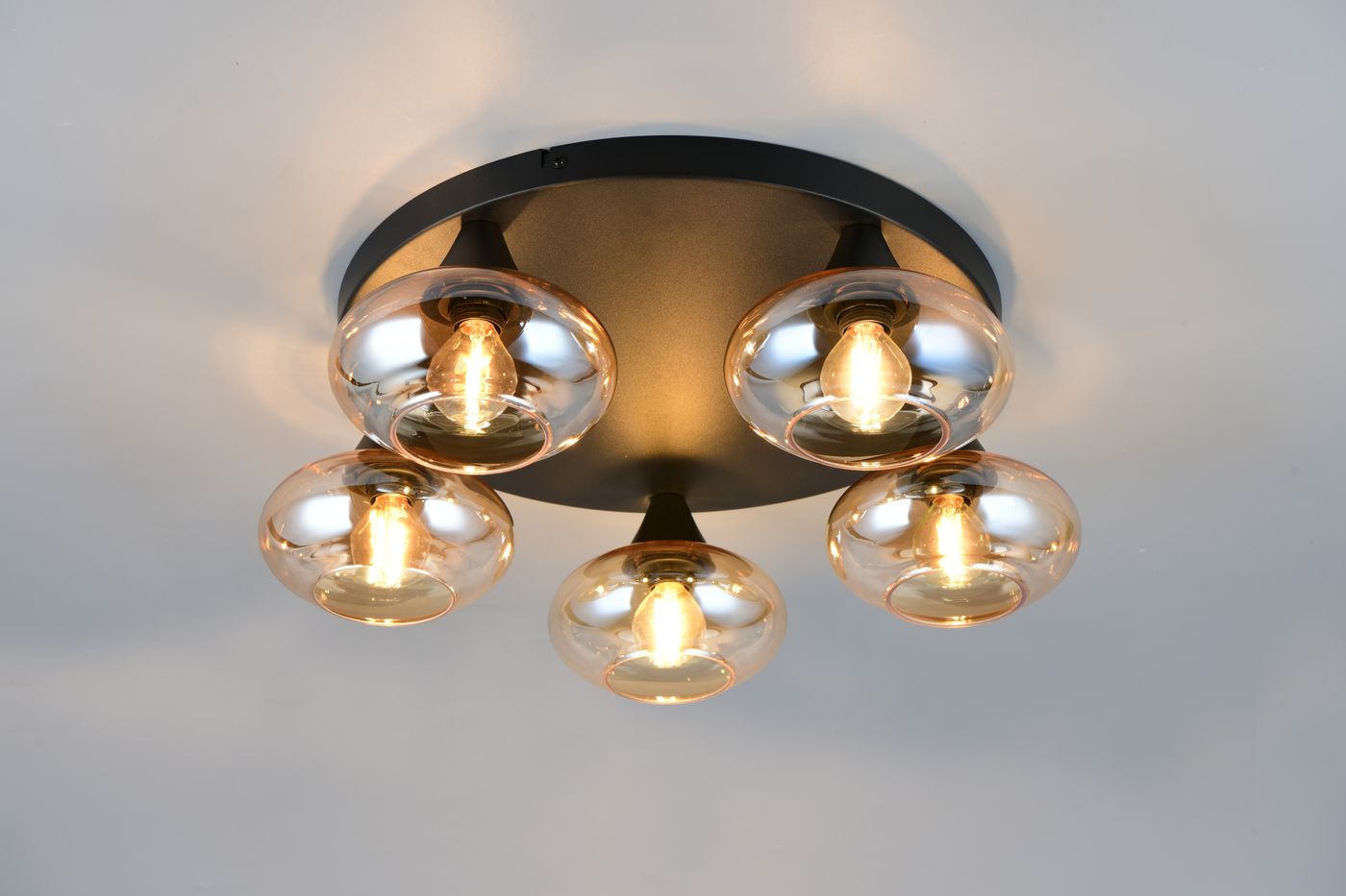 Lampa sufitowa Divina z pięcioma oprawami E14, czarna podstawa, bursztynowe klosze o okrągłym kształcie, zamontowana na suficie. Klosze przezroczyste, widoczne żarówki emitujące ciepłe światło.