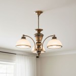 Żyrandol Pelion 3-punktowy O3183 W3 PAT w kolorze mosiądzu z trzema białymi kloszami, zawieszony na suficie. Klosze mają zaokrąglony kształt, a całość ma elegancki, klasyczny styl. Widoczne elementy metalowe i detale dekoracyjne.