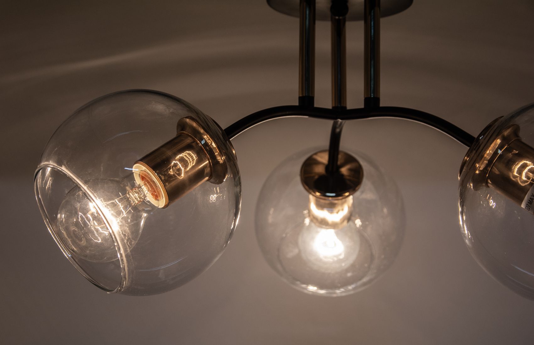 Lampa sufitowa Elba z trzema oprawami E27, w kolorze czarnym i złotym. Szklane klosze w formie kul, metalowe elementy w złotym wykończeniu. Ujęcie z góry, ukazujące detale połączeń i źródła światła. Tło jednolite, subtelne.
