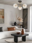 Lampa sufitowa Elba 3xE27 w kolorze czarnym i złotym, z trzema okrągłymi kloszami z przezroczystego szkła. Zamontowana na suficie, w otoczeniu nowoczesnego wnętrza z jasną sofą i czarnym stolikiem.
