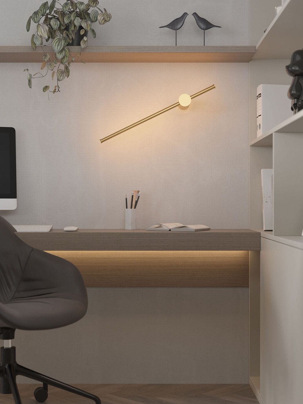 Złoty kinkiet Spirit 1xLED 9W, zamontowany na ścianie, w kształcie poziomej linii z okrągłym źródłem światła. Oświetla biurko z ciemnym krzesłem i rośliną w doniczce na półce. Tło w jasnym kolorze, minimalistyczne.