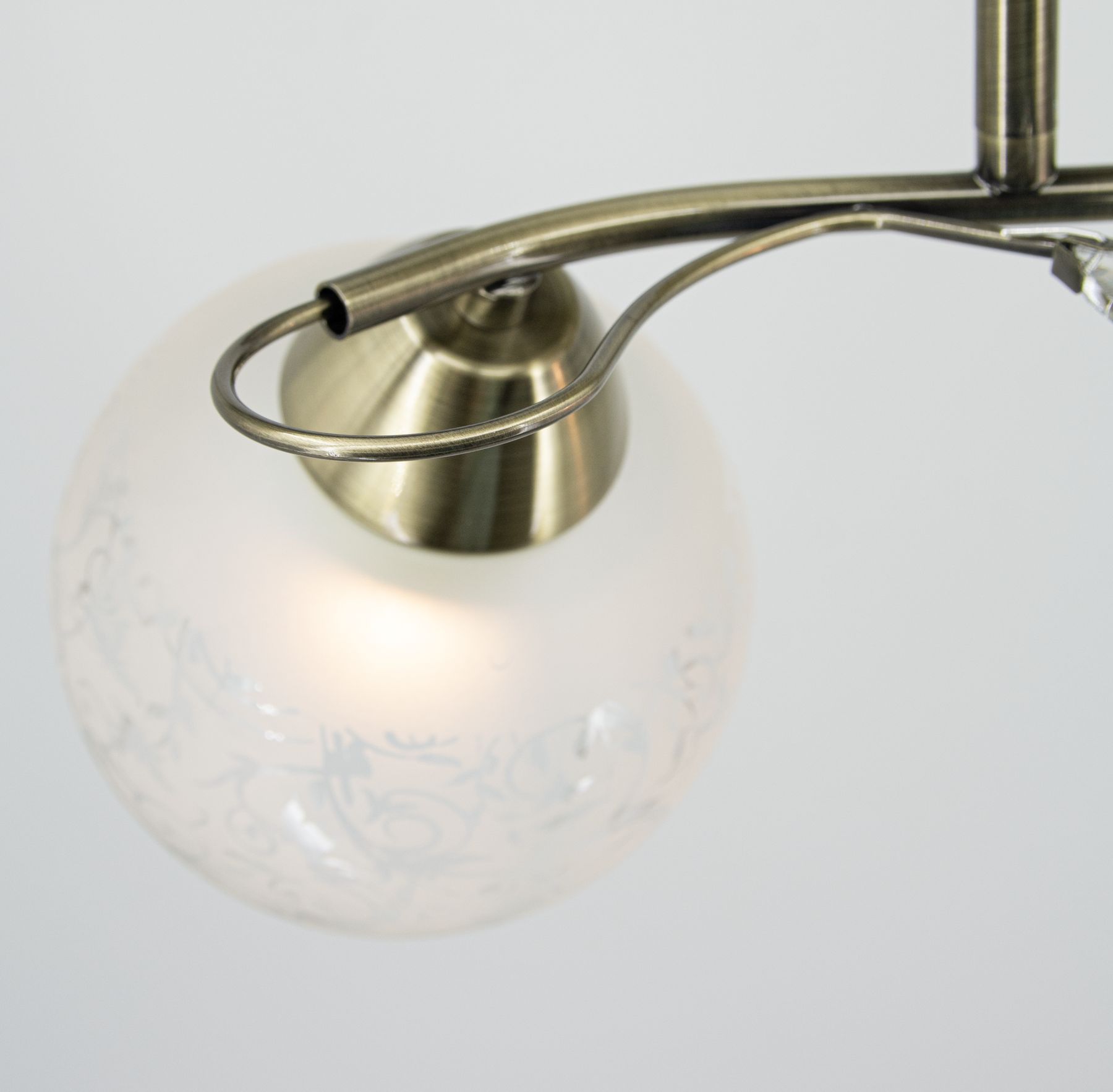 Lampa sufitowa Olivier w kolorze patyny, z dwoma źródłami światła E27. Okrągła, matowa klosz z delikatnym wzorem, zawieszona na metalowym ramieniu. Ujęcie z góry, ukazujące szczegóły konstrukcji i zdobień.