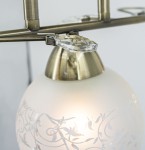 Lampa sufitowa Olivier w kolorze patyny, z trzema oprawami E27. Posiada szklane klosze z matowym wykończeniem i dekoracyjnym wzorem. Zbliżenie na detale mocowania i kryształowe elementy ozdobne.