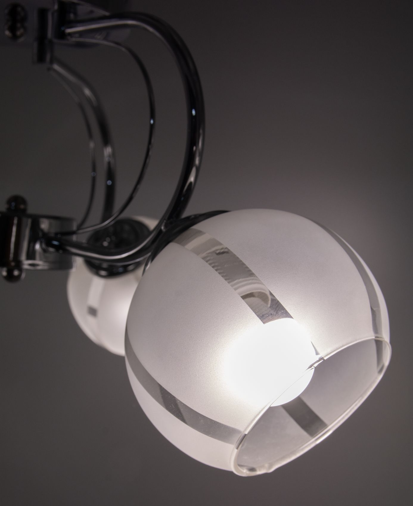 Lampa sufitowa Ruby z trzema kloszami E27 w chromowanej oprawie. Klosze o półprzezroczystej fakturze z metalicznymi paskami, zamontowane na elastycznych ramionach, widok z boku w zbliżeniu. Tło ciemne, podkreślające design lampy.