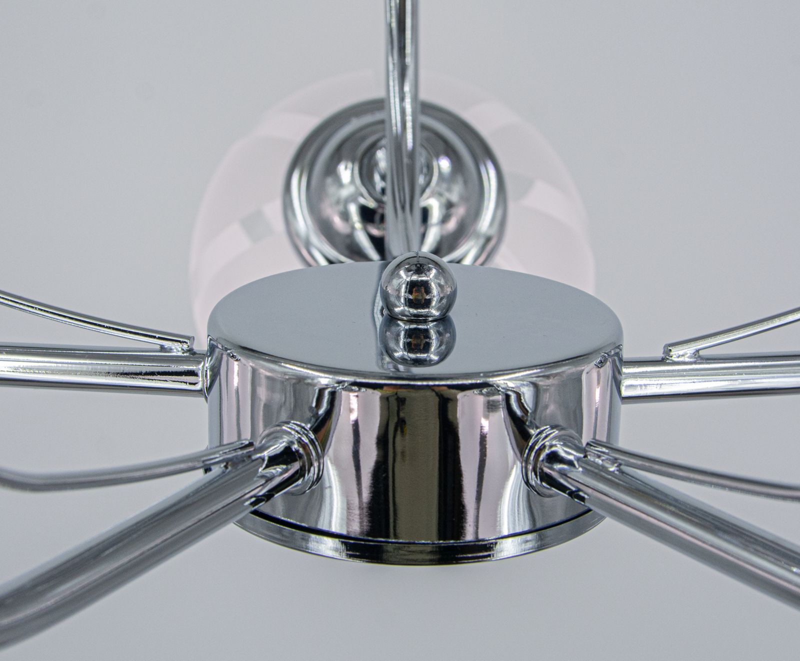 Lampa sufitowa Ruby z chromowanym wykończeniem, z pięcioma ramionami na żarówki E27. Ujęcie z dołu, ukazujące centralną część oraz błyszczące metalowe elementy. Tło białe, co podkreśla refleksy świetlne.