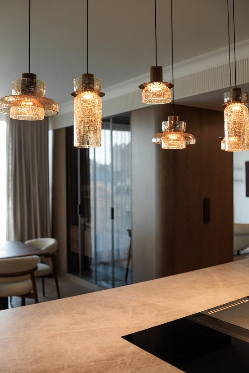 Lampa wisząca Signature z jednym źródłem LED 8W w kolorze mosiądzu, z pięcioma szklanymi kloszami o strukturze crackle, zwisająca nad blatem kuchennym. Ujęcie z boku, ukazujące elegancki design i ciepłe światło.